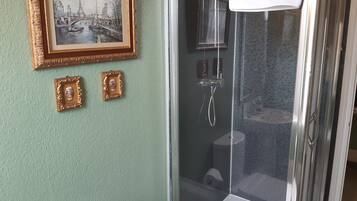 Ett badrum med en dusch som är avskärmad med glasväggar, en toalett och ett handfat. Det finns två inramade tavlor på väggen.