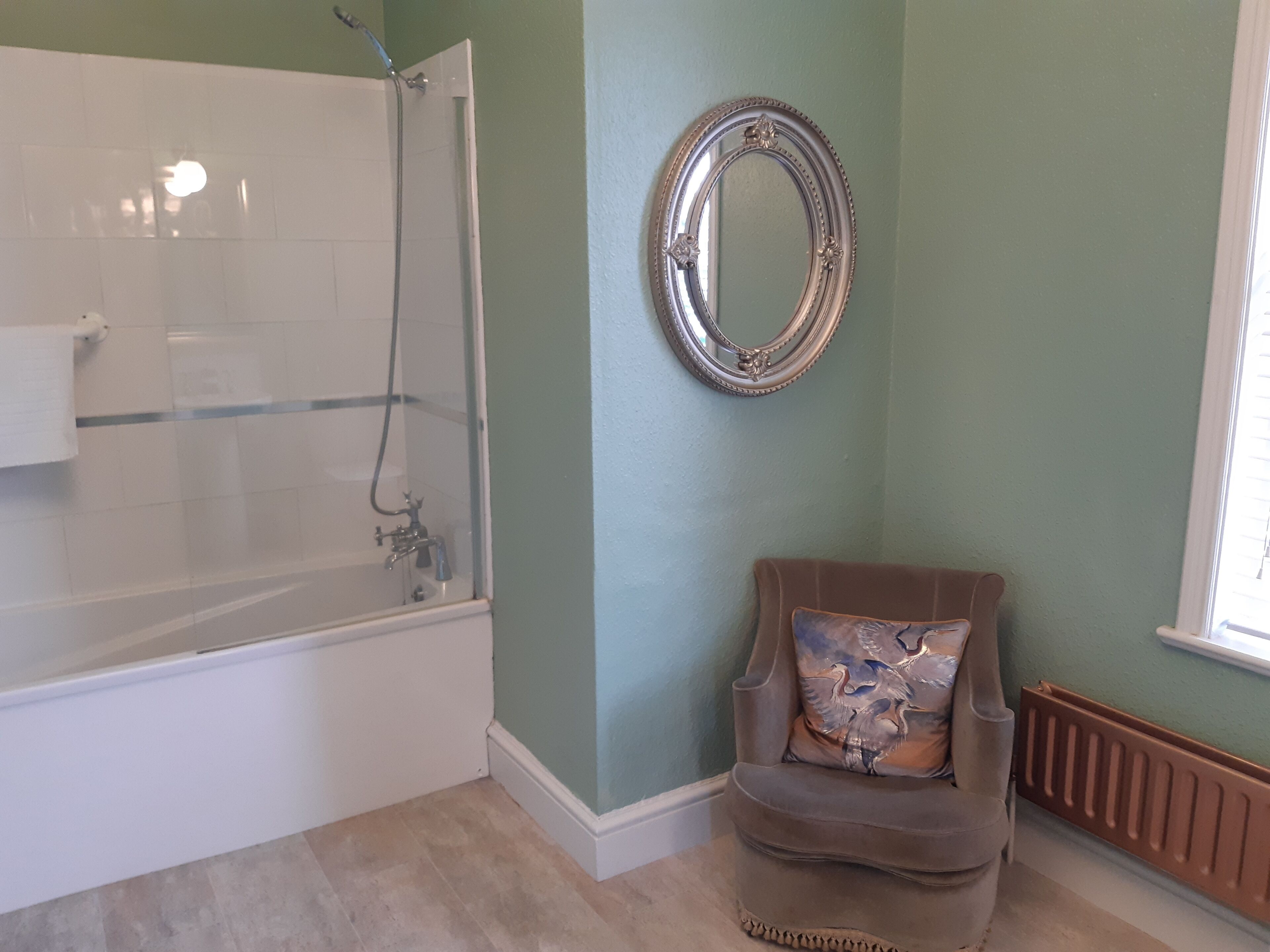 Un baño con bañera, ducha, una silla con cojín decorativo y un espejo en la pared.