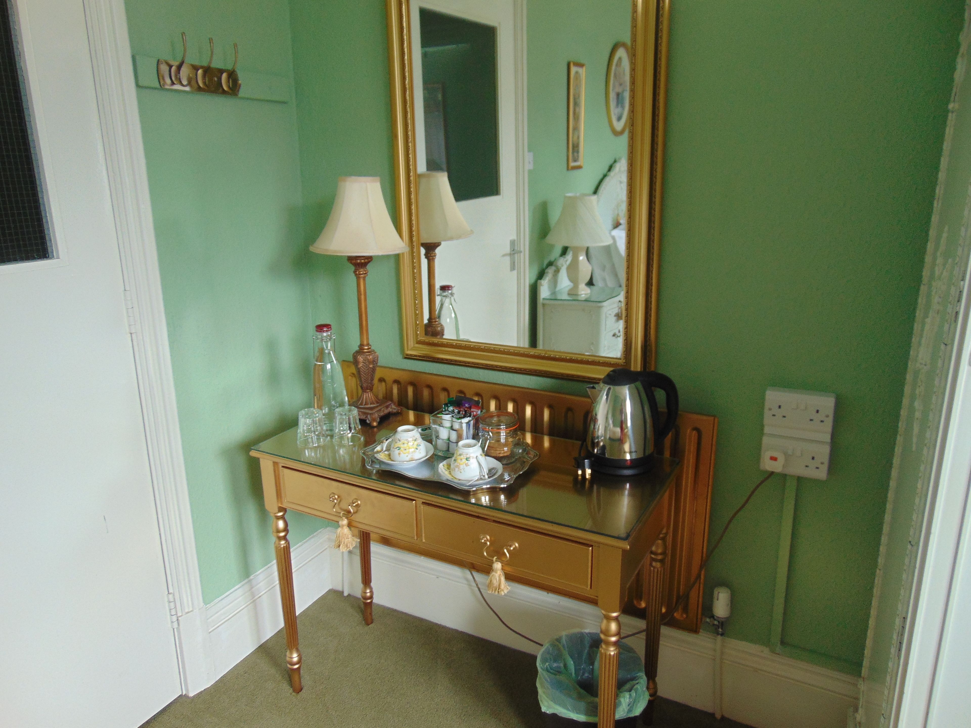 Une pièce avec un mur vert, une table en bois surmontée d’une plaque de verre, un miroir et une bouilloire.