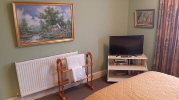 A bedroom with a bed, a radiator, a wooden towel rack, a television on a stand, and two framed pictures on the wall.