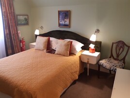 Una habitación de hotel con cama, mesitas de noche, una silla, un extintor y un cuadro en la pared.