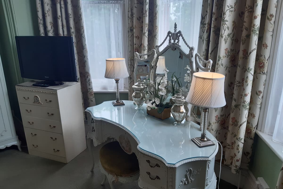 A vintage-style vanity with ornate details, a television on a cabinet, and floral curtains.