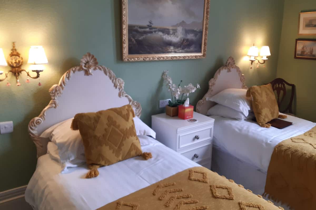 A hotel room with two beds, a nightstand, a painting on the wall, and wall sconces.