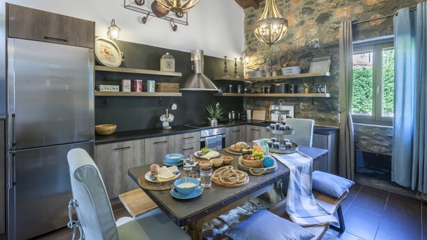 Una cocina moderna con pared de piedra, electrodomésticos de acero inoxidable y un comedor con mesa puesta para una comida.