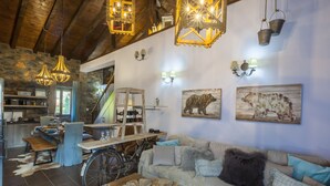 Un interior rústico con techo de madera, paredes de piedra, zona de comedor y un sofá con cojines.