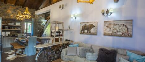 A rustic interior with a wooden ceiling, stone walls, a dining area, and a sofa with cushions.