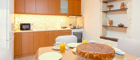 A breakfast setup with a cake, orange juice, and toast on a table in a kitchen with wooden cabinets and a tiled backsplash.