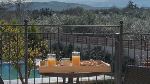 En balkon med et bord dækket til morgenmad, med udsigt over et bjergrigt landskab.