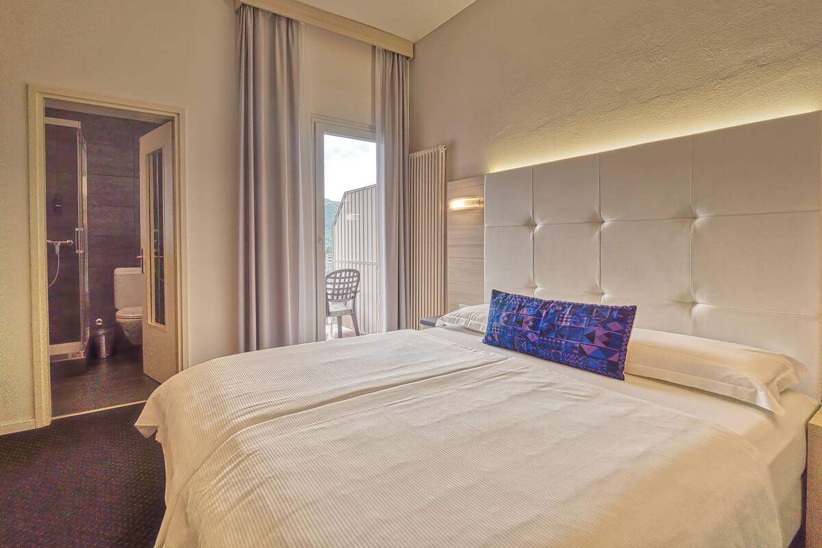 A hotel room with a large bed, a bathroom with a shower, and a view of the outdoors.