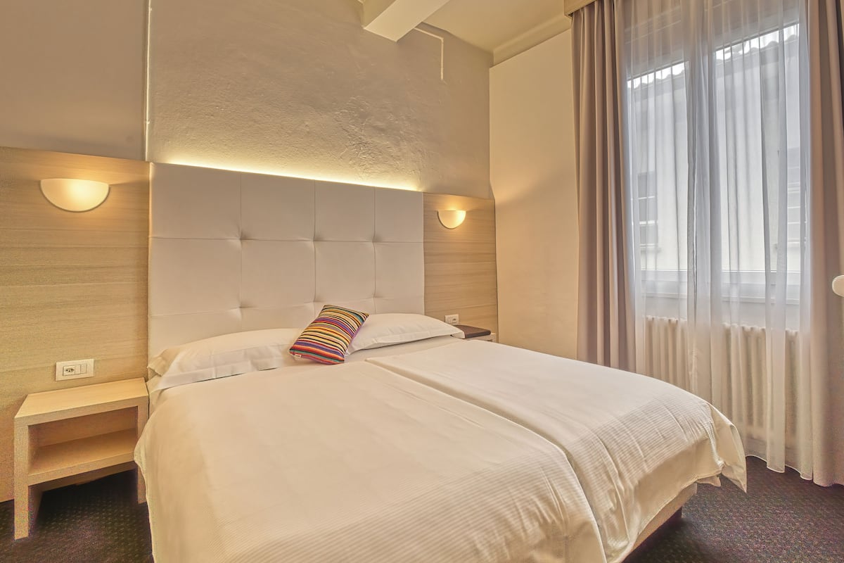 A hotel room with a large bed, two bedside tables, and a headboard with built-in lighting.