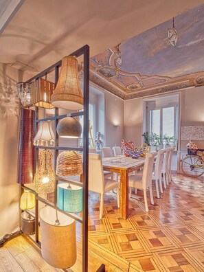 A dining area with a wooden table, white chairs, and a patterned floor. - @ Home Hotel Locarno (Muralto)