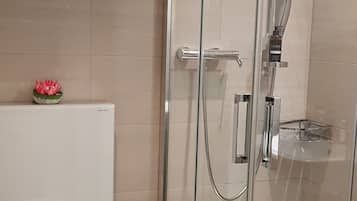 A modern bathroom with a glass-enclosed shower, a toilet, and a trash bin.