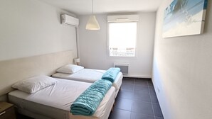 Une petite chambre propre, avec deux lits, une fenêtre donnant sur un beau paysage, un luminaire au plafond et un appareil de climatisation.