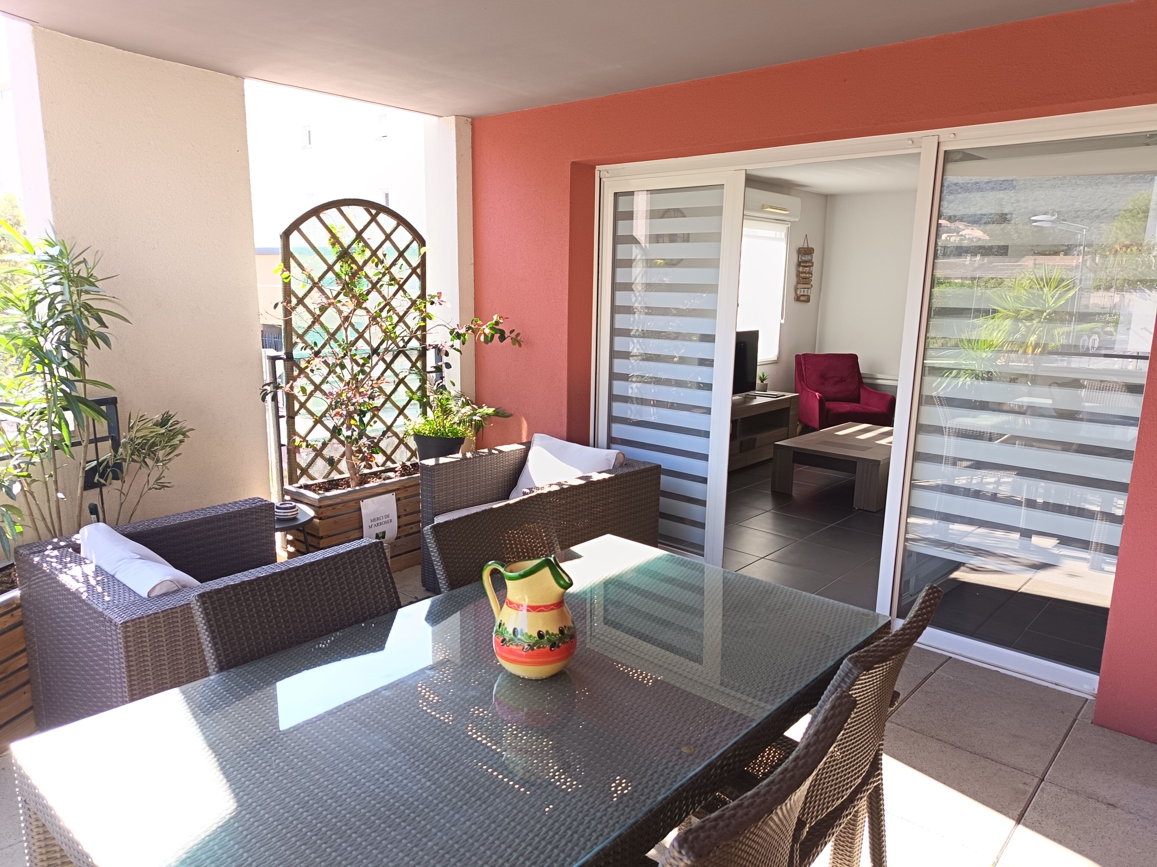 A patio with wicker furniture, a glass table, and a potted plant.