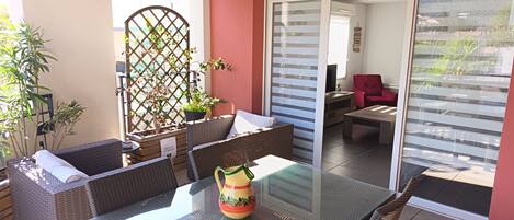 A patio with wicker furniture, a glass table, and a potted plant.