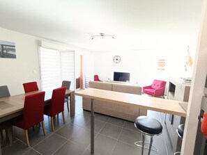 A modern living space with a dining area, sofa, TV, and a kitchen area.