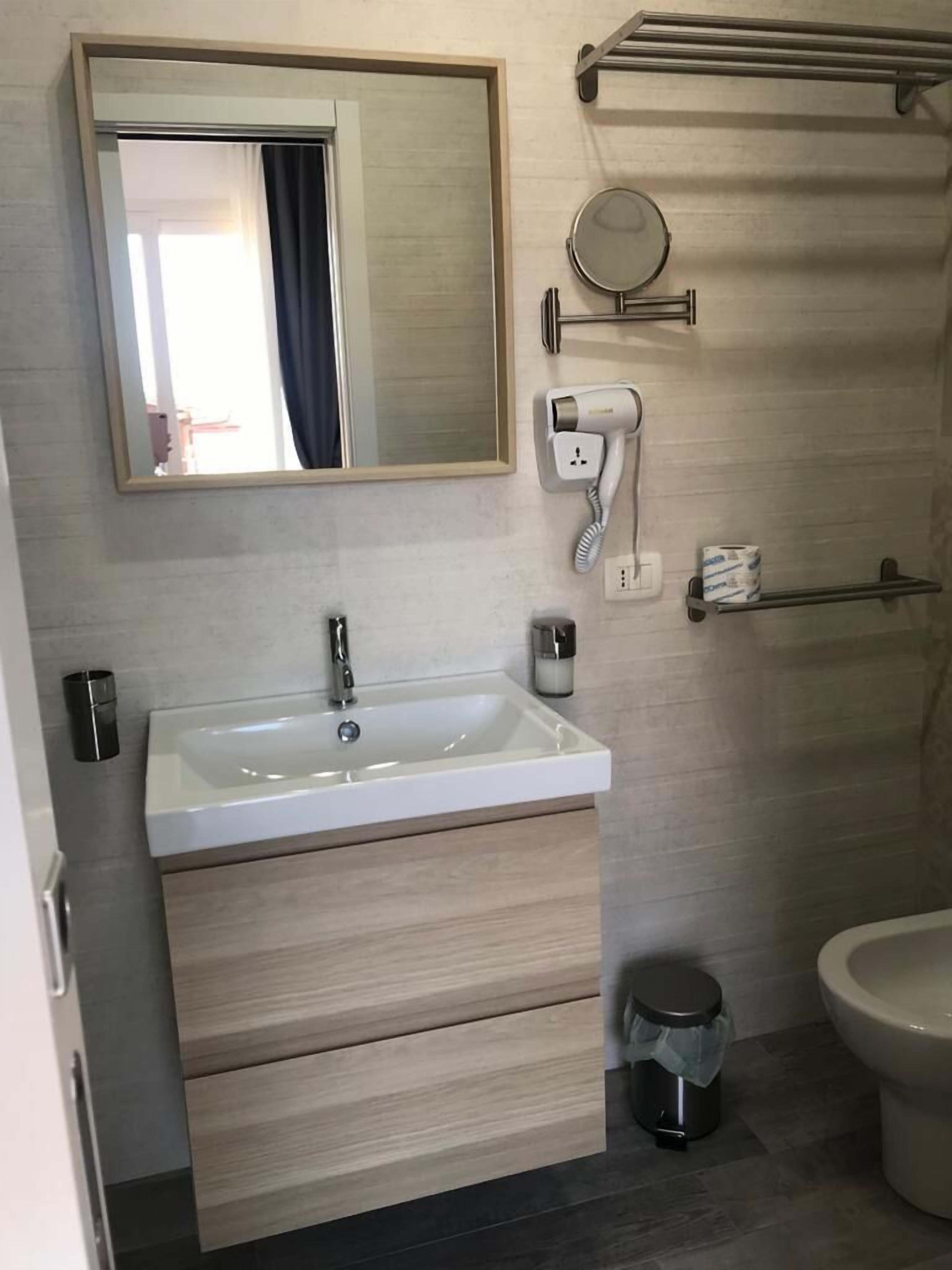 A bathroom with a white sink, a mirror, a hairdryer, a toilet, and a trash bin.
