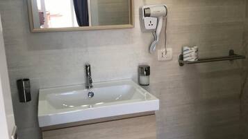 A bathroom with a white sink, a mirror, a hairdryer, a toilet, and a trash bin.