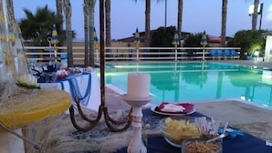 Ein Tisch am Pool mit einem weißen Kerzenleuchter, einer Obstschale und einem Glas Nüsse.