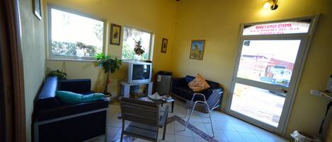 Una sala de estar con sofá, televisor, una mesita y ventana con vistas al exterior.