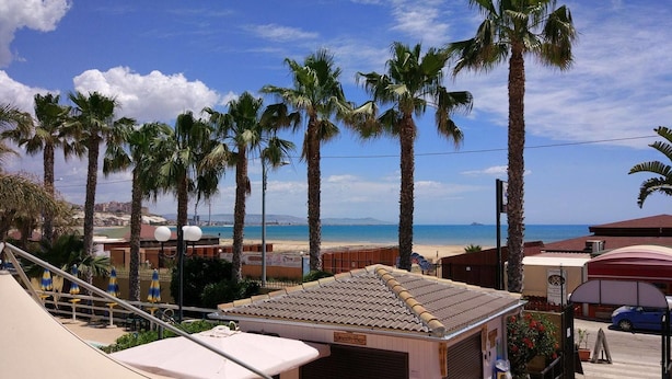 Ein Strandimbiss mit Ziegeldach, Sitzgelegenheiten im Freien und Blick auf Strand und Meer.