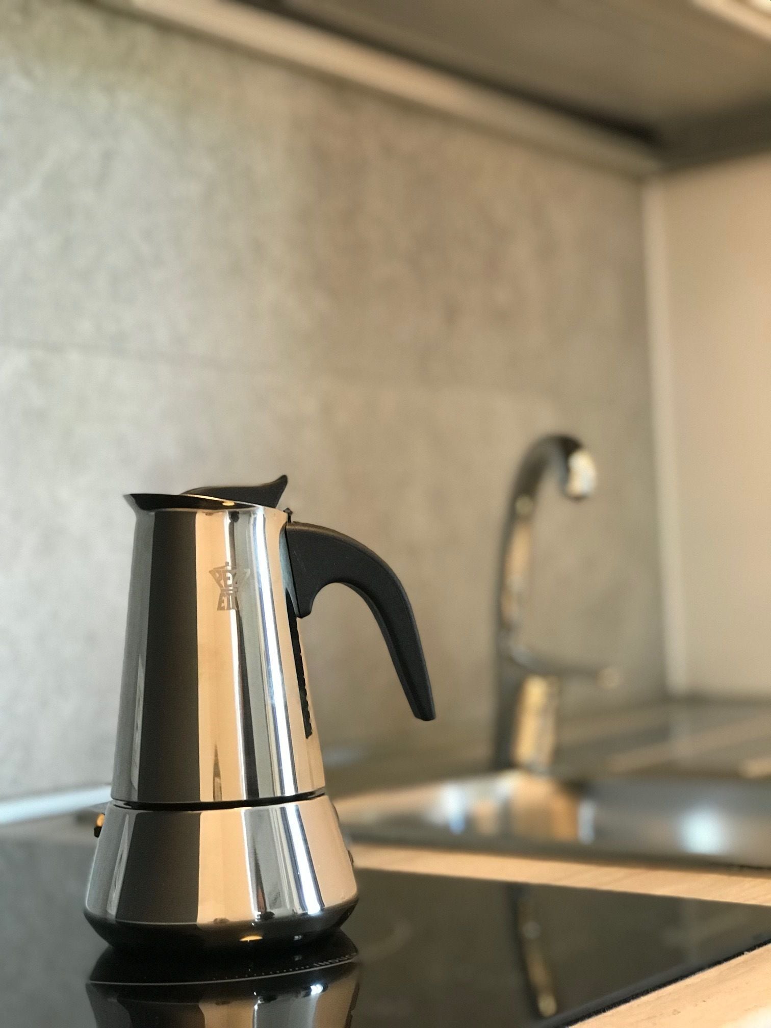 A stainless steel kettle on a black countertop with a modern kitchen backsplash and a faucet in the background.