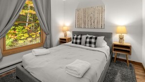 A bedroom with a large bed, two bedside tables with lamps, a window with curtains, and a wall-mounted artwork. - 57 North Lynx 3 Bedroom Condo by RedAwning (Warren)