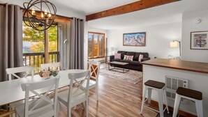 A modern living room with a wooden ceiling, a sofa, a dining table with chairs, and a kitchen area with a bar stool. - 57 North Lynx 3 Bedroom Condo by RedAwning (Warren)