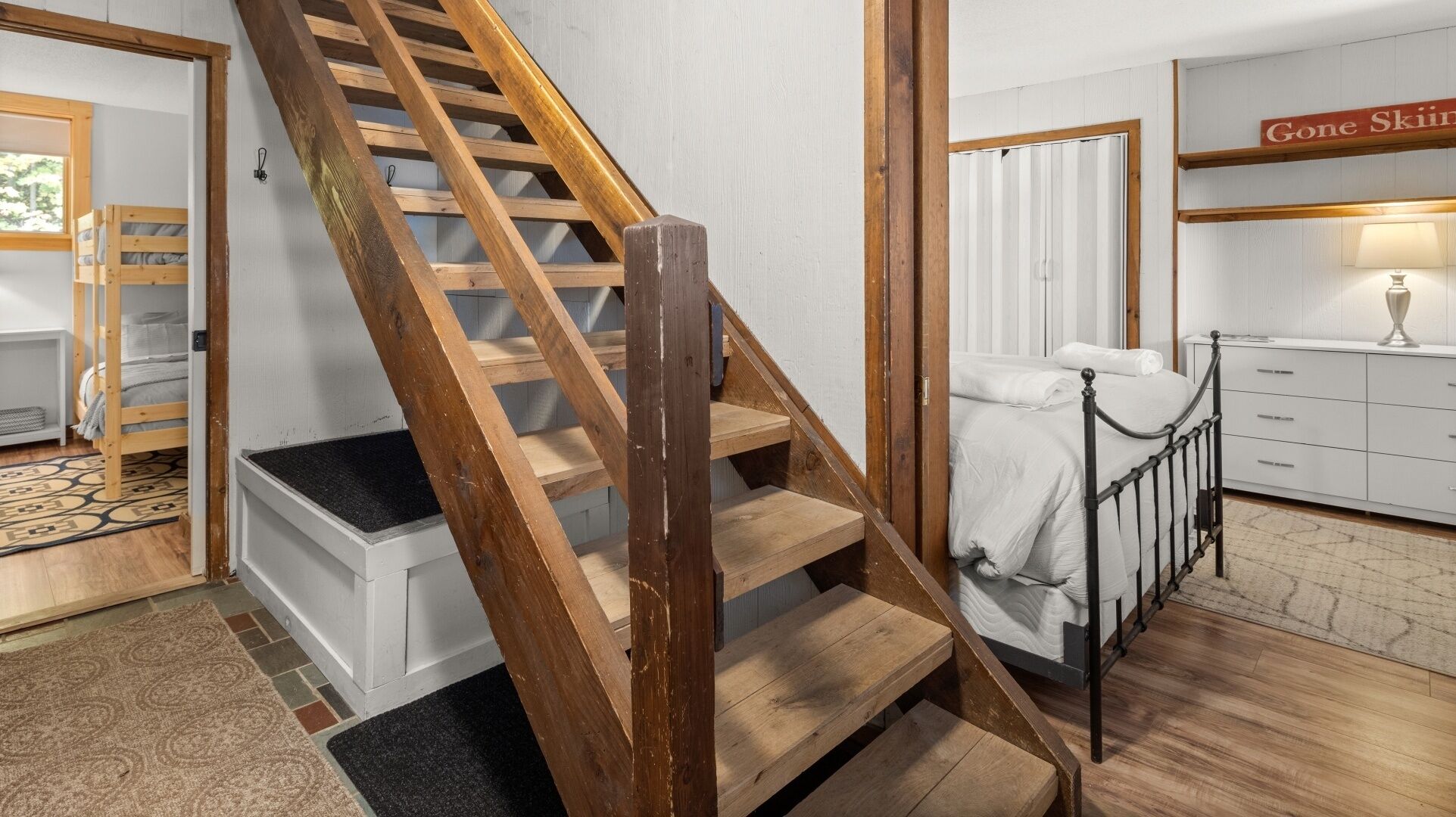A staircase with wooden steps and a metal handrail, leading to a bedroom with a bed and a dresser.
