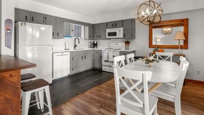A modern kitchen with white appliances, grey cabinets, and a dining area with white chairs and a wooden table. - 57 North Lynx 3 Bedroom Condo by RedAwning (Warren)