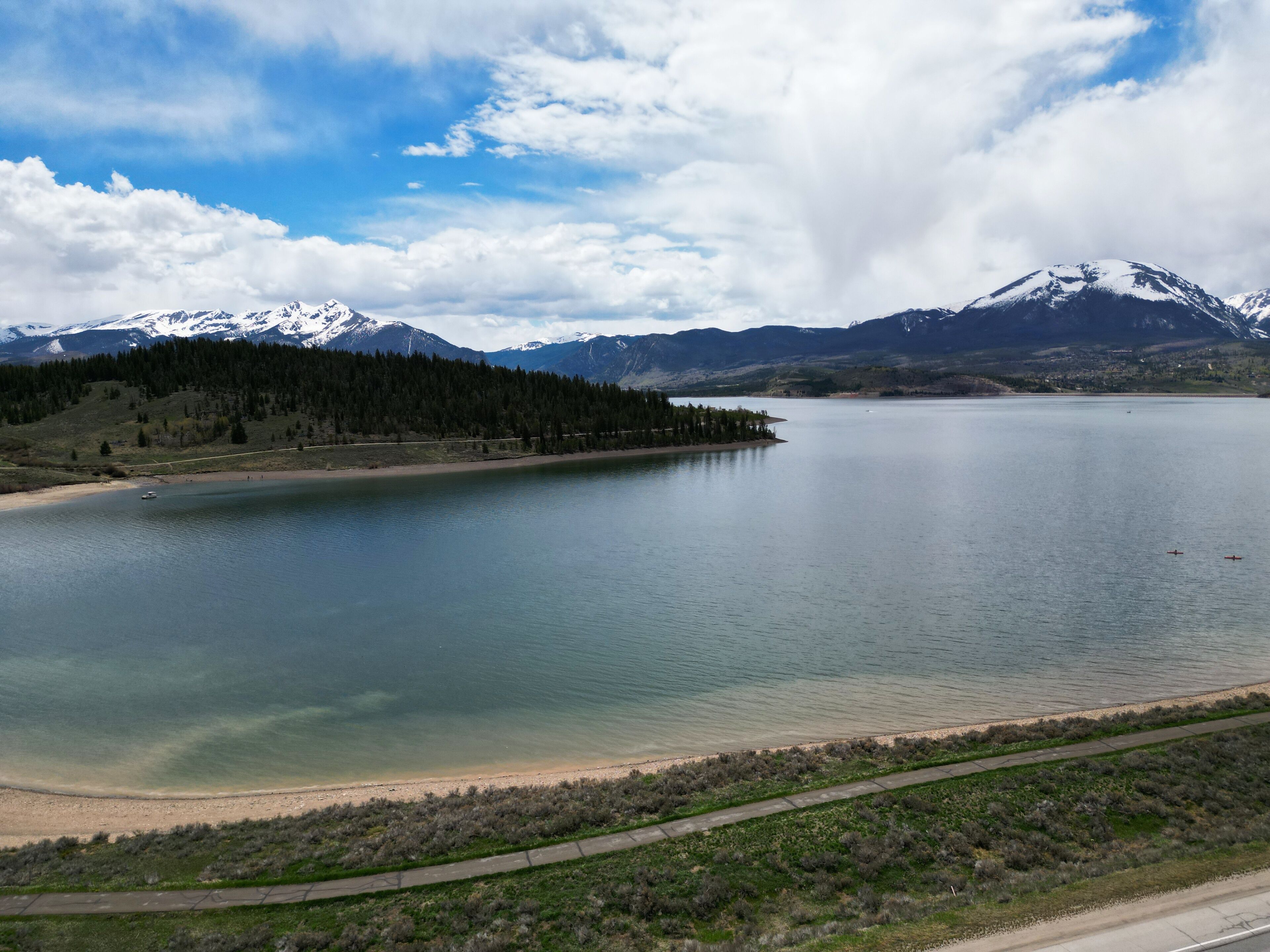 A lake with a road alongside, surrounded by mountains and a forest.