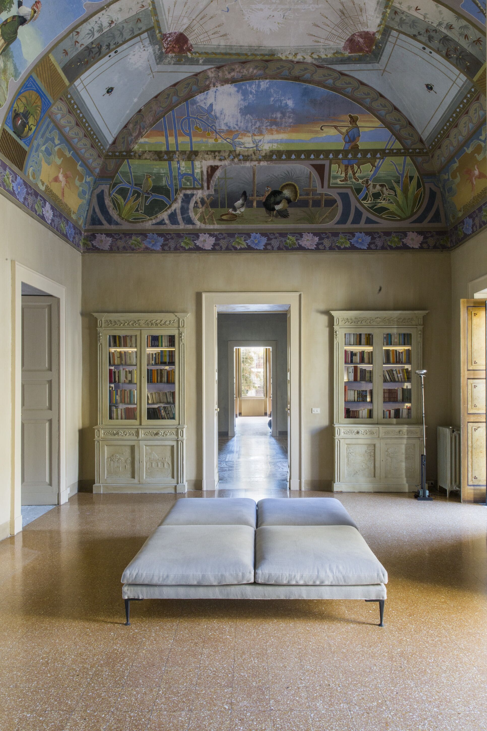 Una habitación amplia con una cama grande, dos libreros y un mural en el techo.
