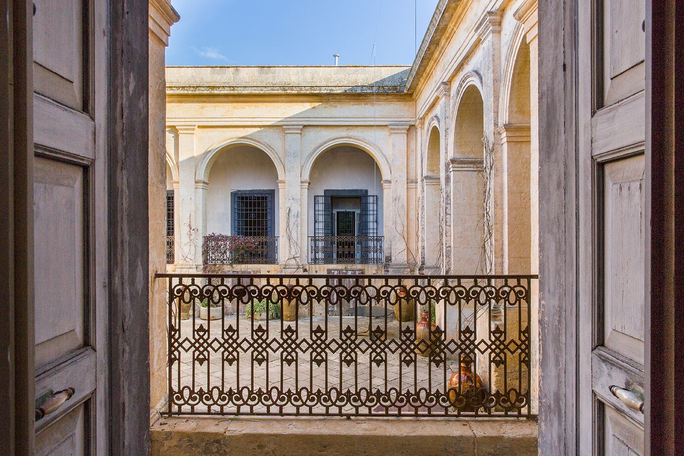 A courtyard with a balcony, featuring a wrought iron railing and a view of a building with arches and windows.
