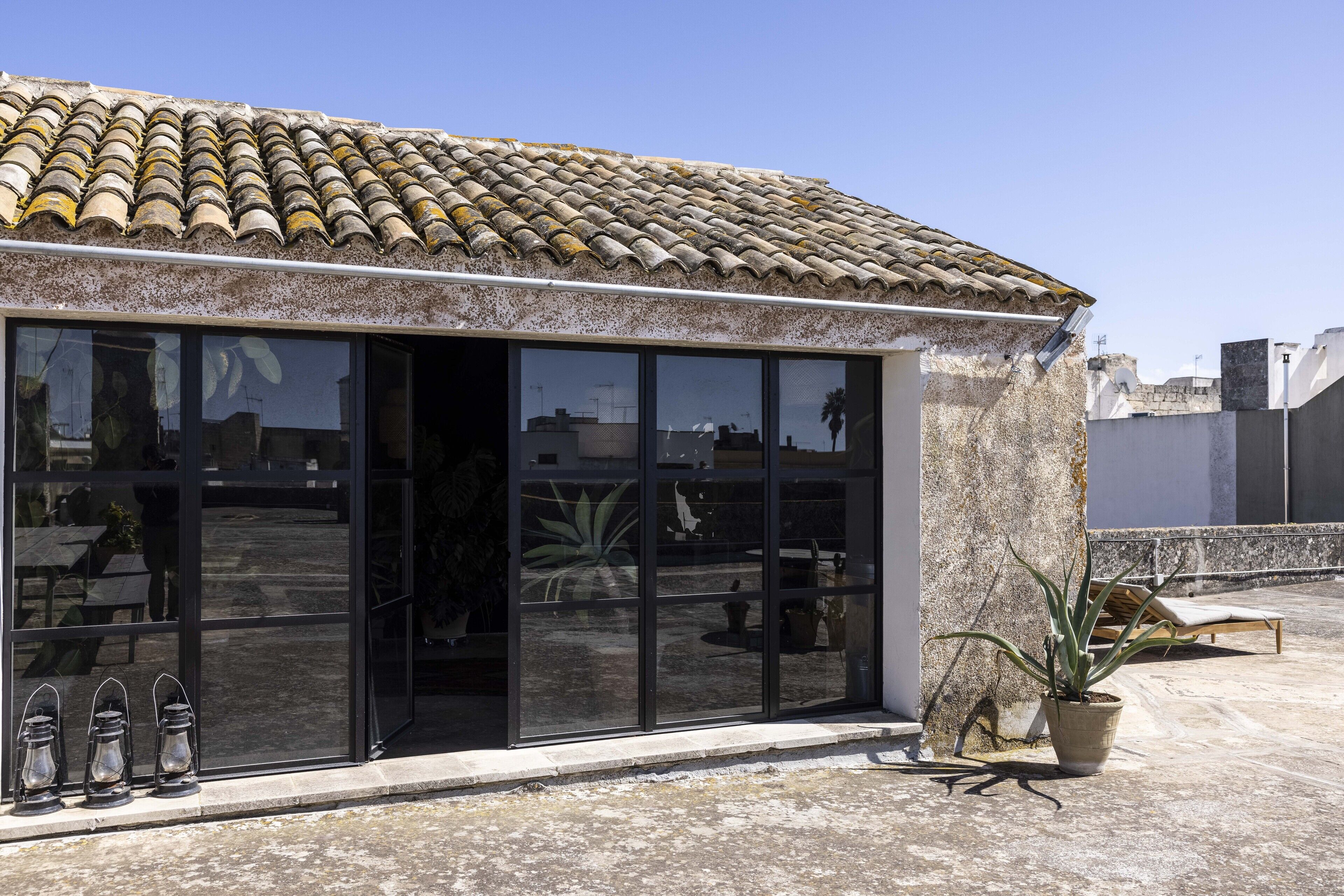 A building with a tiled roof, large glass windows, and potted plants on the terrace.