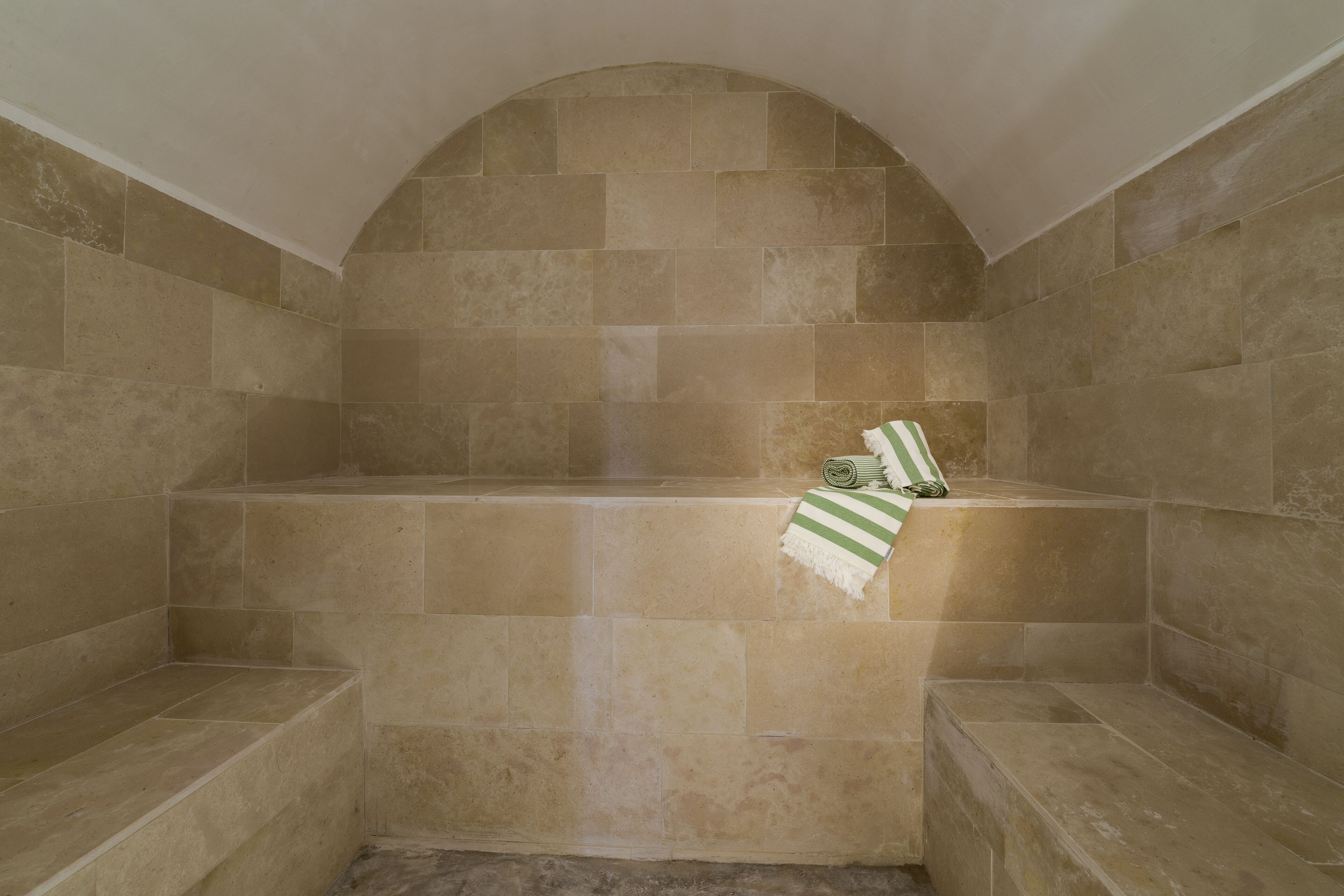 A bathroom with beige tiles, a bathtub, and a towel on the edge.