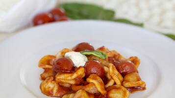 Eine Portion Pasta mit cremiger Soße und Cocktailtomaten, dazu eine Schüssel weißer Käse und ein Gewürzmühle.