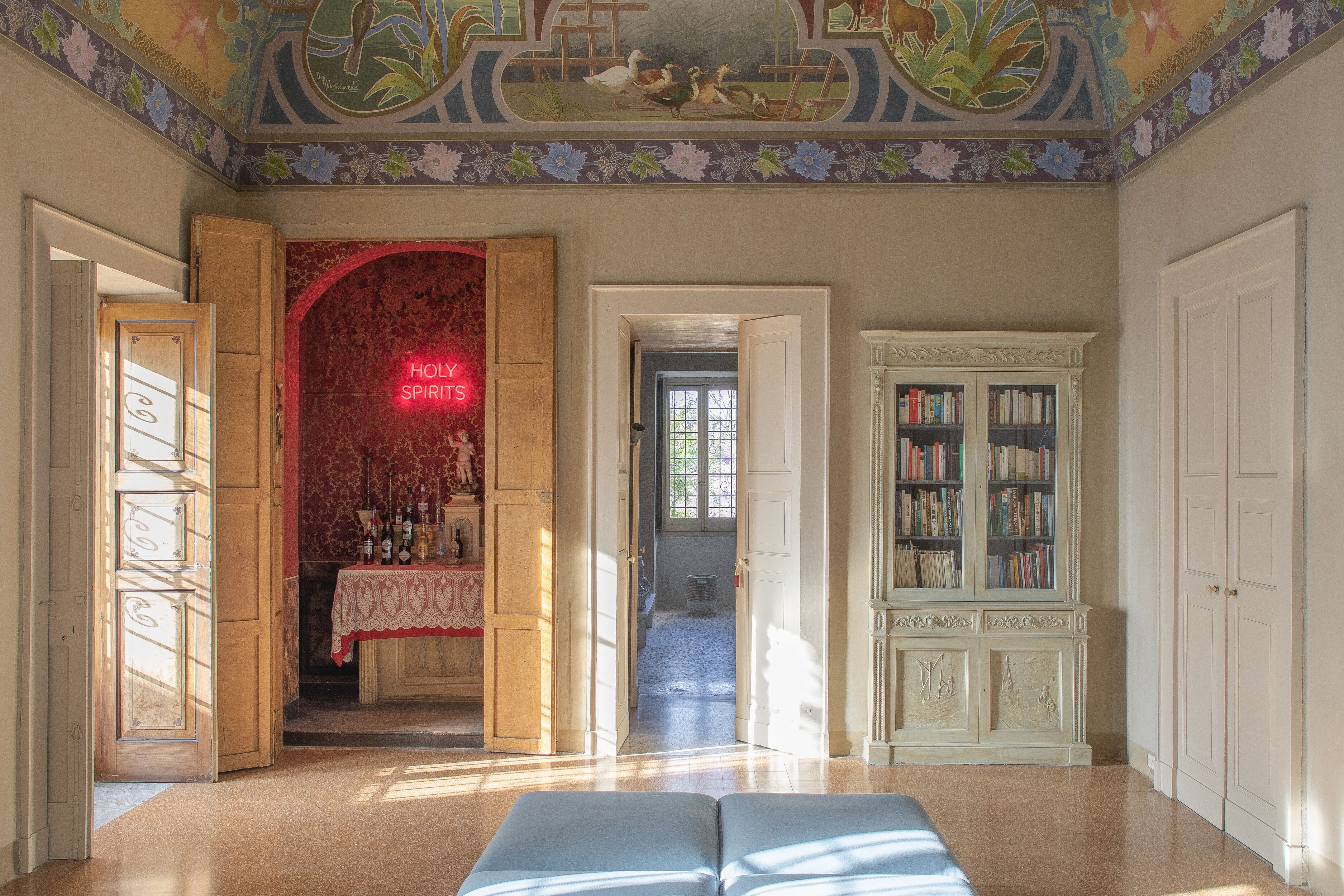 A room with a large open area, a red-lit alcove, a bookshelf, and a view through an open door.
