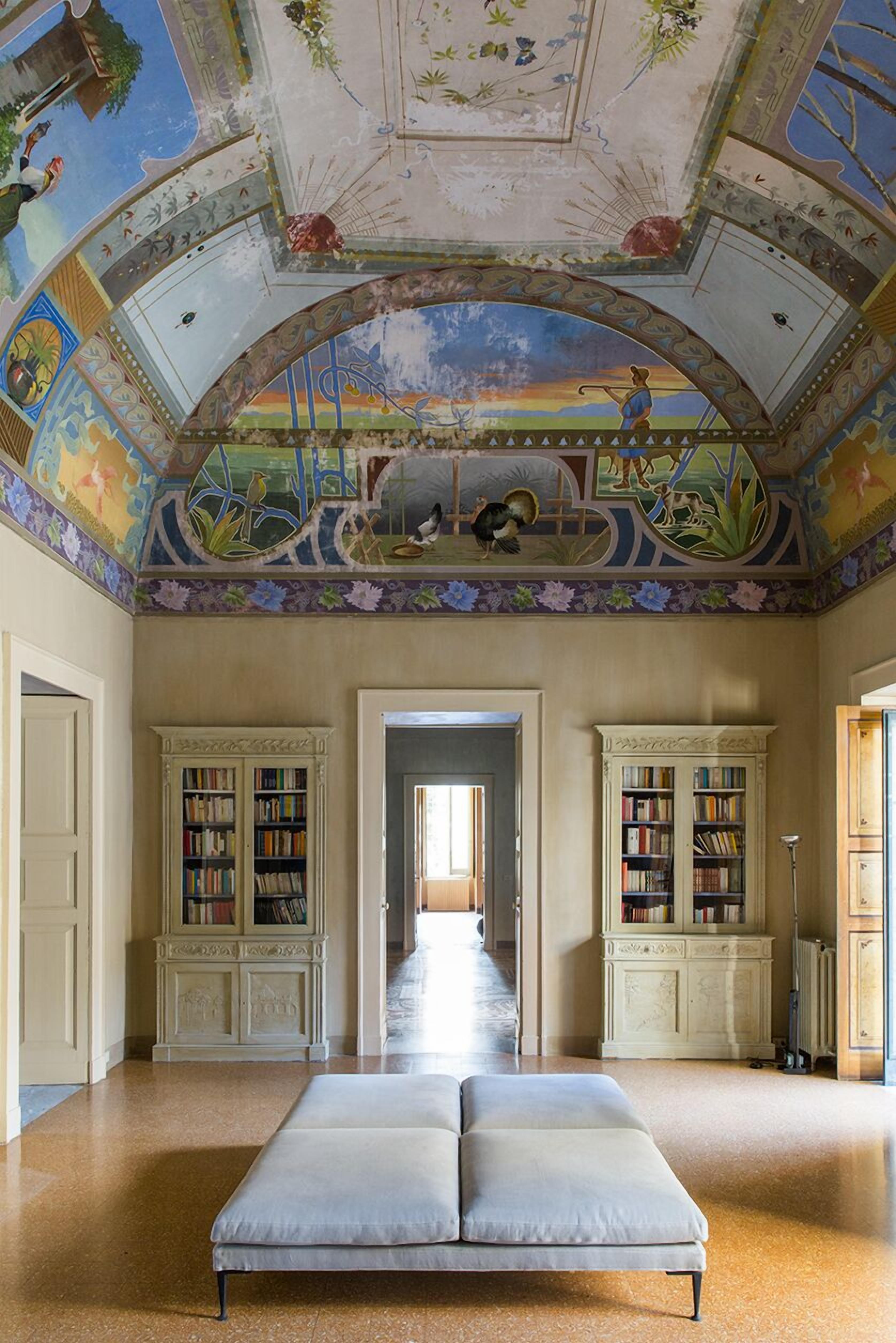 Una habitación con una cama grande, dos estanterías y un techo decorado con murales detallados.