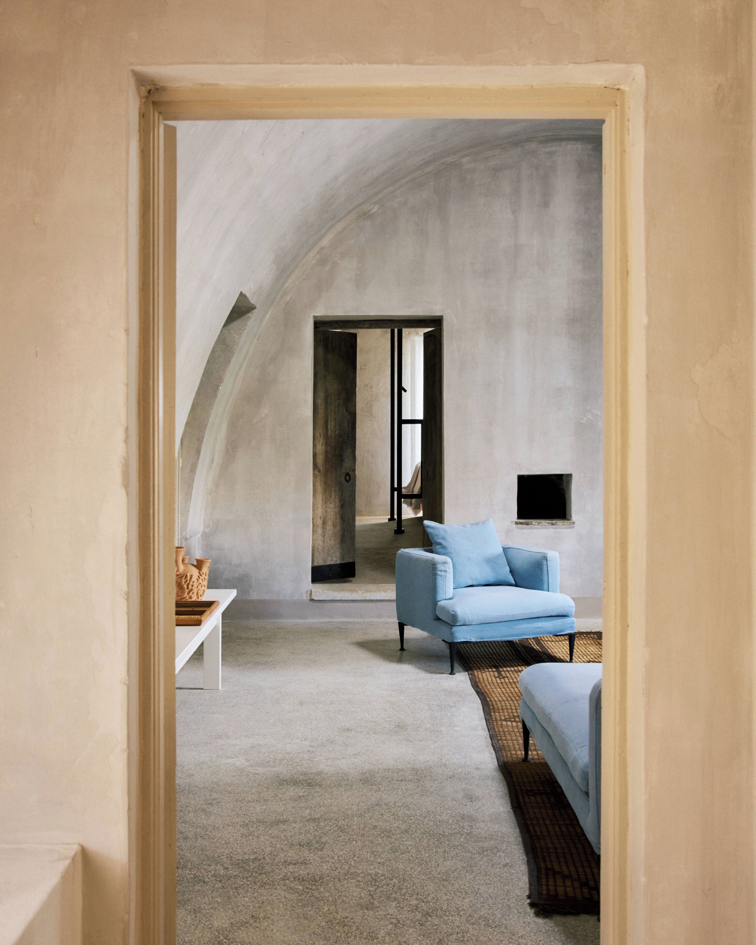 Ein Zimmer mit einer hohen gewölbten Decke, einem hellblauen Sofa, einem kleinen Tisch und einem an der Wand befestigten Fernseher.