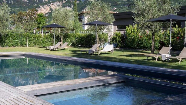 A swimming pool with lounge chairs and umbrellas, surrounded by greenery and a mountainous backdrop. - Verdepiano Bed&Camping (Riva del Garda)