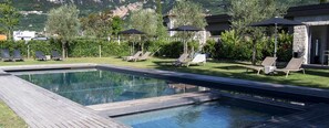 Une piscine entourée de chaises longues et de parasols, bordée de verdure et avec une chaîne de montagnes en toile de fond.