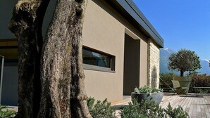 A modern building with a beige exterior, a large window, and a paved patio area with outdoor furniture and potted plants. - Verdepiano Bed&Camping (Riva del Garda)