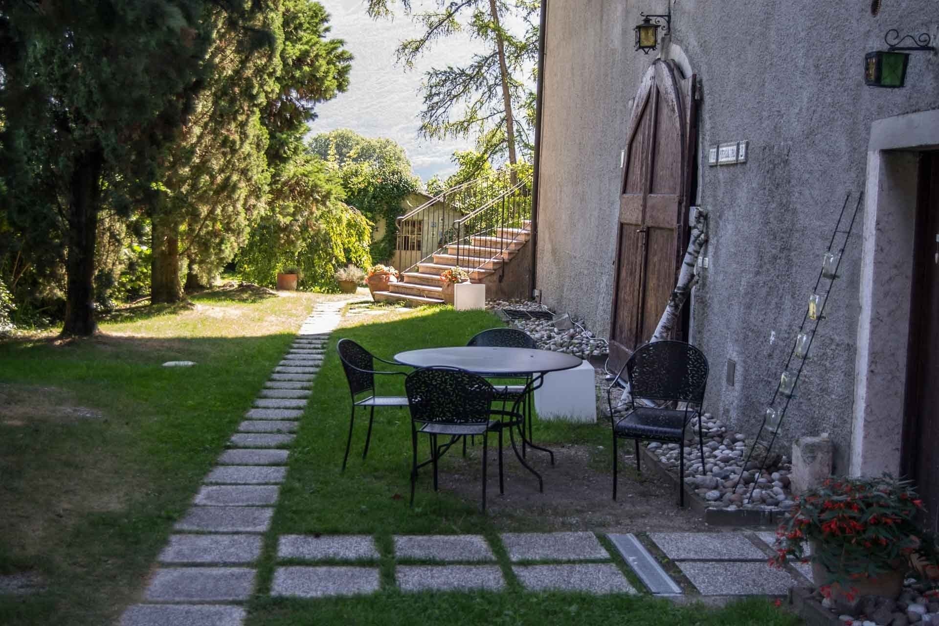 Un patio con tavolo e sedie, un vialetto in pietra e vista su una scalinata che conduce a un edificio.