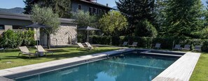 Una piscina rectangular con solárium de madera, rodeada de sillas de descanso y sombrillas.