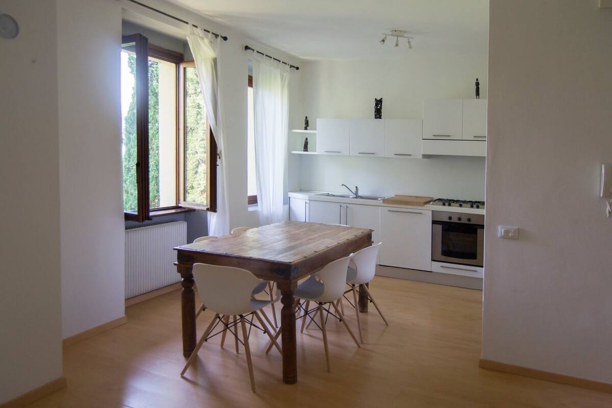 Une cuisine moderne avec des meubles blancs, une table à manger en bois et un four encastré.