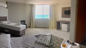 A hotel room with a bed, a desk, a TV, and a window with a view of the sea. - Happy Hotel Pajuçara (Maceió)