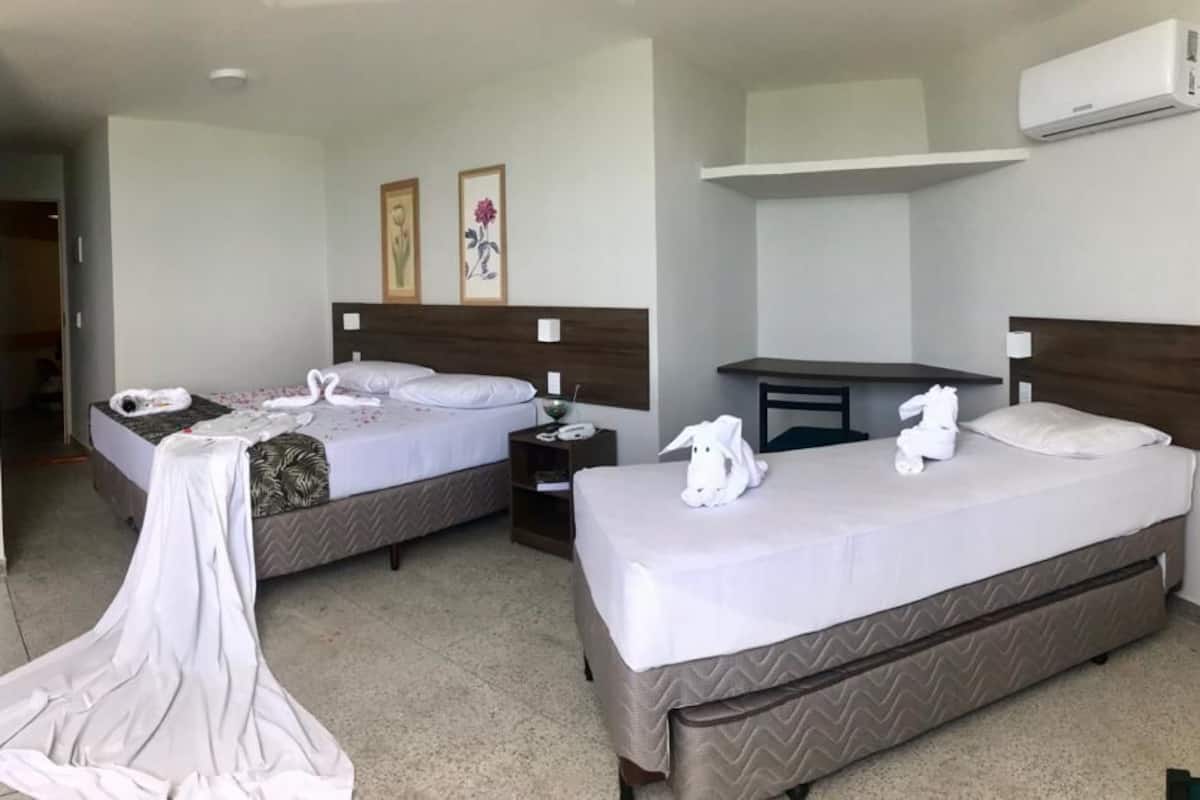 A hotel room with two beds, a desk, a chair, a nightstand, and an air conditioning unit.