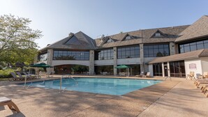 A pool area with lounge chairs and umbrellas, a stone building with large windows, and a clear sky.
