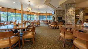 A spacious dining area with high ceilings, large windows, and stone walls. Tables and chairs are arranged for dining.