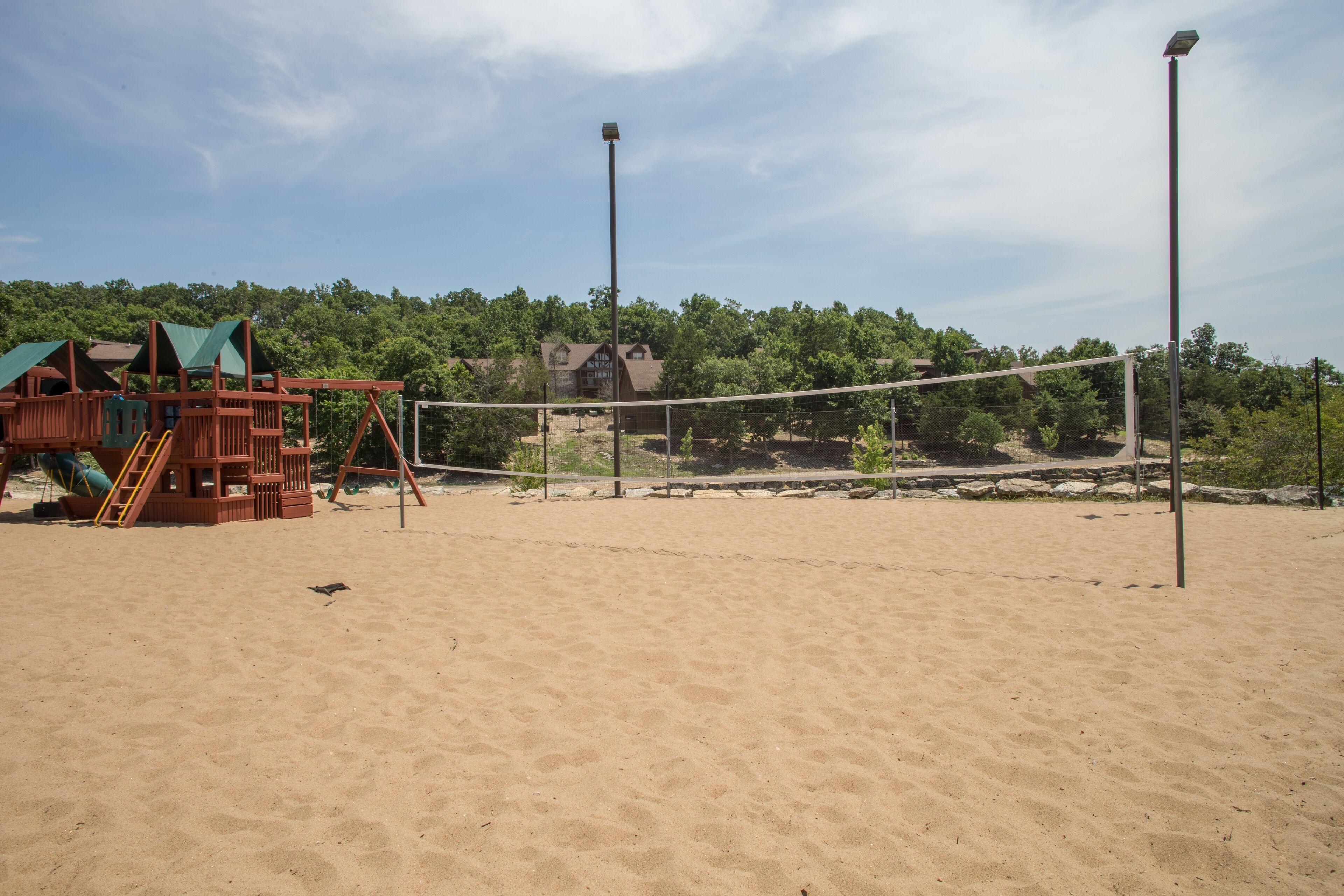 En sandstrand med ett volleybollnät, en lekställning i trä och en byggnad i bakgrunden.